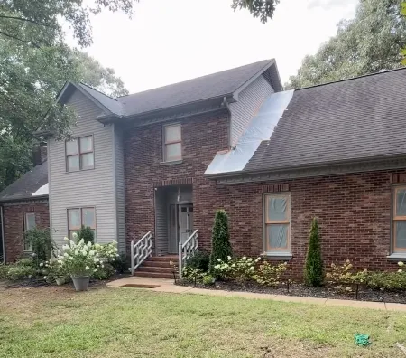 Two story red brick home with grey siding and white railings before painting